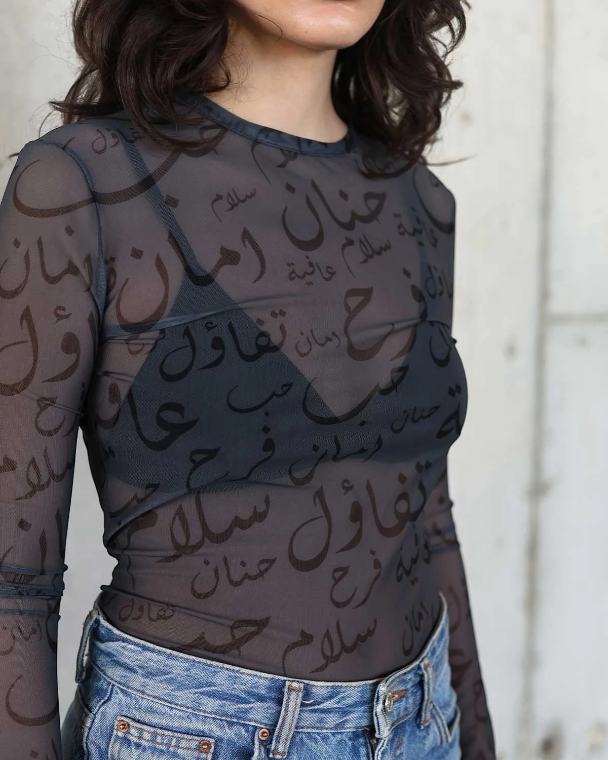 Farah Daylac black sheer mesh long sleeve top with Arabic calligraphy print. Crew neck.