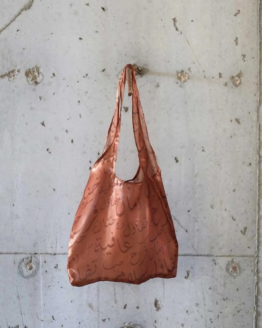 Farah Daylac burnt copper sheer tote bag with Arabic calligraphy print. Features words like tenderness, safety, joy, peace, and wellbeing.