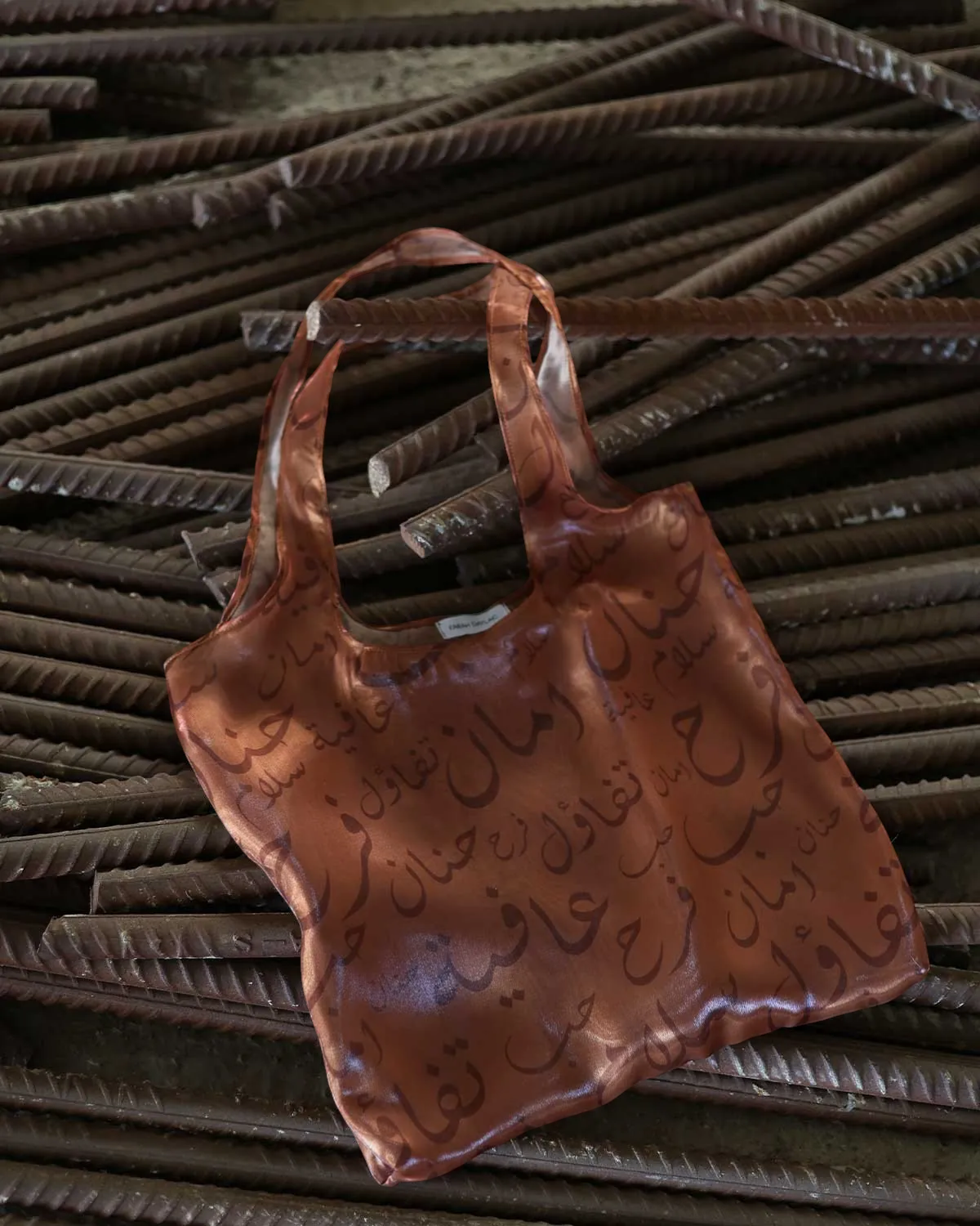 Farah Daylac burnt copper sheer tote bag with Arabic calligraphy print. Features words like tenderness, safety, joy, peace, and wellbeing.