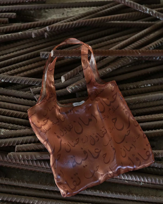 Farah Daylac burnt copper sheer tote bag with Arabic calligraphy print. Features words like tenderness, safety, joy, peace, and wellbeing.