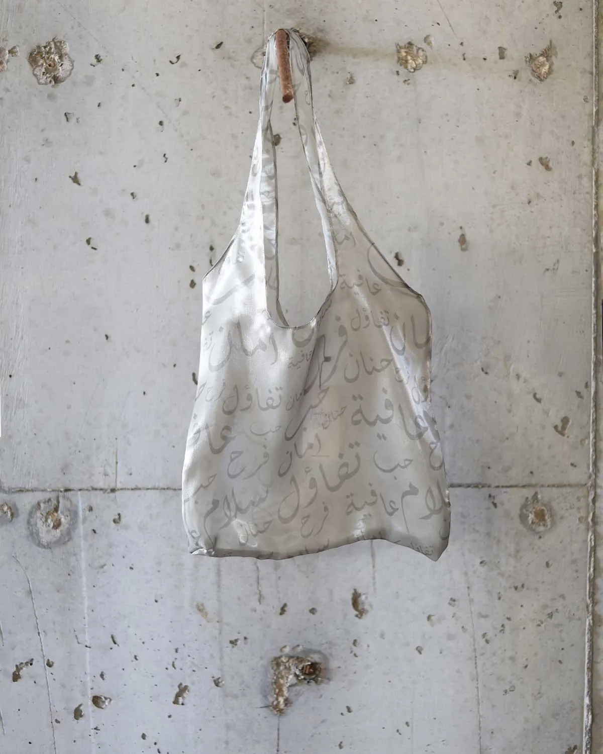 Farah Daylac silver pearl sheer tote bag with Arabic calligraphy print. Features overlapping words like peace, joy, and safety.